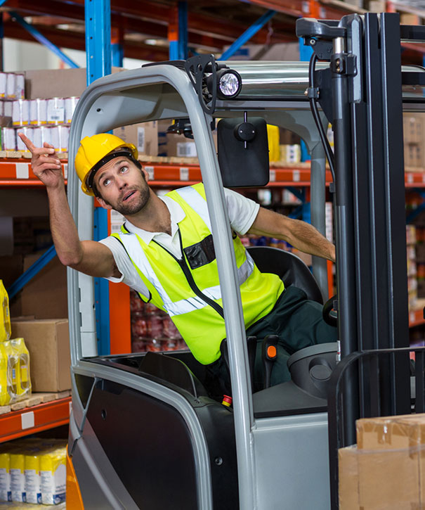 Forklift operator in a yellow hard hat and high-visibility vest working in a warehouse aisle